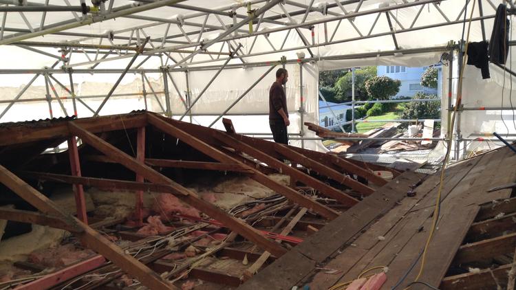 Under a white plastic covered scaffolding is a historic wooden roof, partially dismantled, as a construction site.